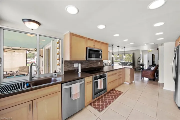Kitchen featuring stainless steel appliances, light brown cabinetry, hanging light fixtures, and sink