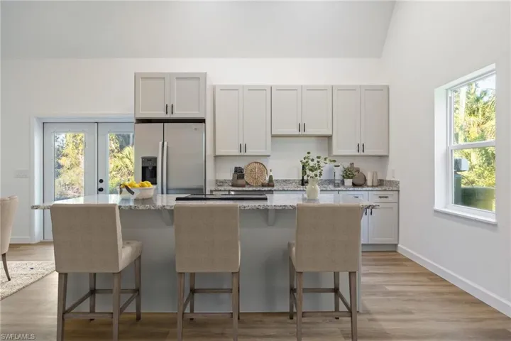Kitchen featuring light stone countertops, stainless steel refrigerator with ice dispenser, a center island with sink, light wood-style floors, and a breakfast bar