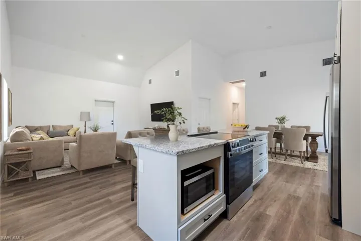 Kitchen with stainless steel appliances, open floor plan, an island with sink, dark wood-style floors, and light stone countertops