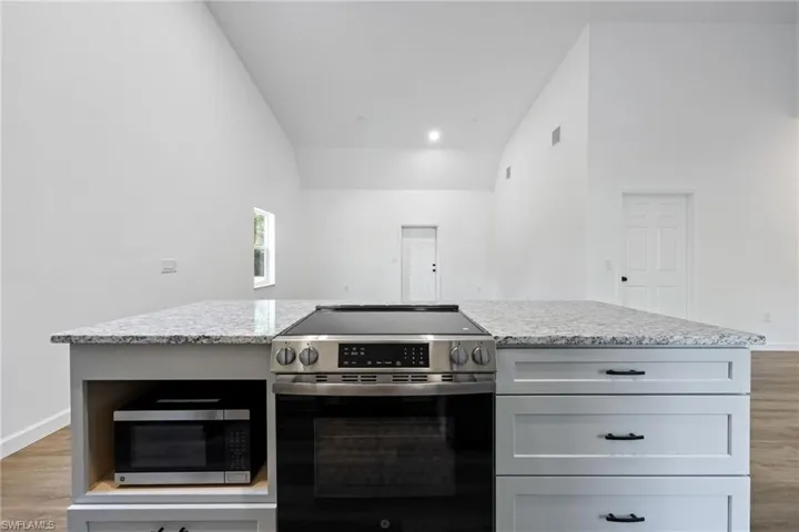 Kitchen featuring stainless steel appliances, light wood-style floors, a center island, light stone counters, and high vaulted ceiling