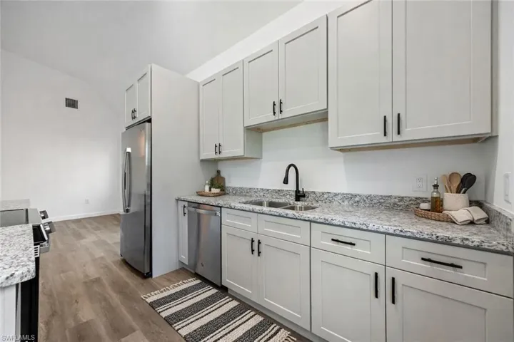 Kitchen featuring stainless steel appliances, light stone countertops, dark wood finished floors, and lofted ceiling