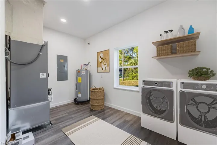 Laundry area with electric panel, dark wood-type flooring, heating unit, water heater, and separate washer and dryer