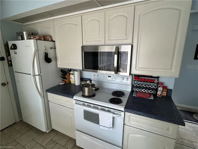 Kitchen with white appliances, light tile patterned flooring, and white cabinetry