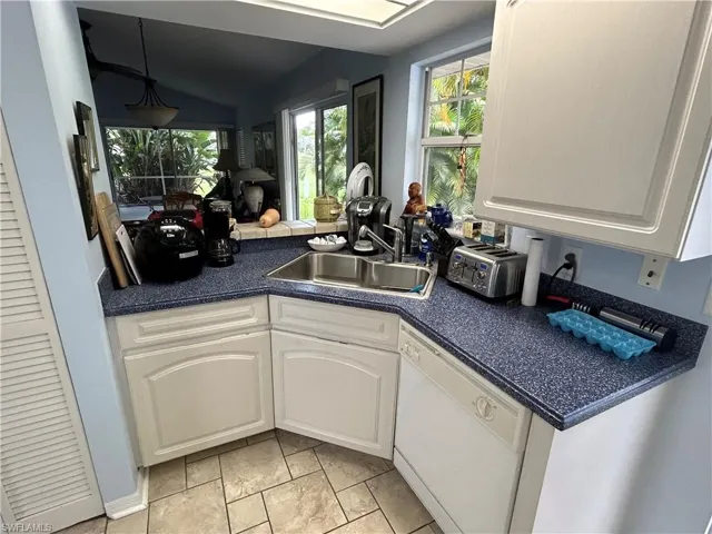 Kitchen featuring vaulted ceiling, white cabinetry, dishwasher, light tile patterned floors, and sink