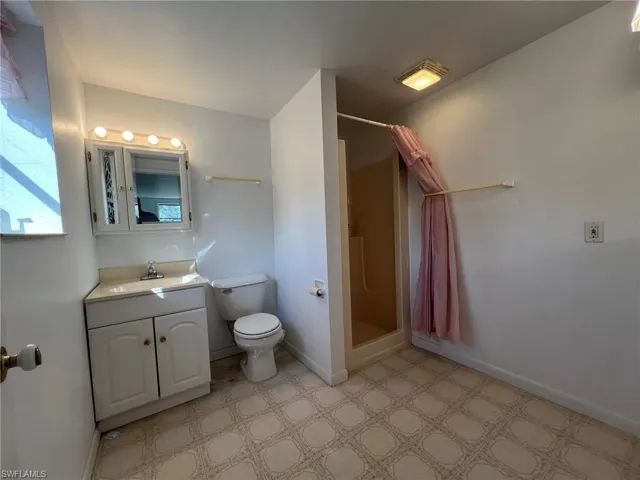 Bathroom with toilet, vanity, baseboards, tile patterned floors, and a stall shower