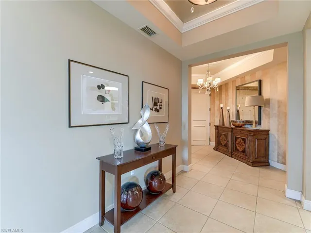Corridor with ornamental molding, light tile patterned flooring, a tray ceiling, and suspended lighting