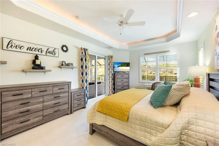 Primary bedroom showcasing tray ceilings, recessed lighting, and sliding glass doors opening to the screened lanai. What an amazing way to wake up every morning. You may not want to get out of bed.