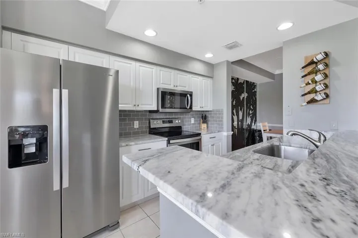 Kitchen with appliances with stainless steel finishes, a sink, light stone countertops, white cabinetry, and light tile patterned flooring