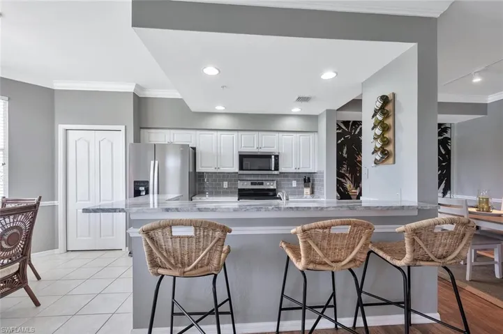 Kitchen featuring appliances with stainless steel finishes, crown molding, a kitchen breakfast bar, decorative backsplash, and white cabinets