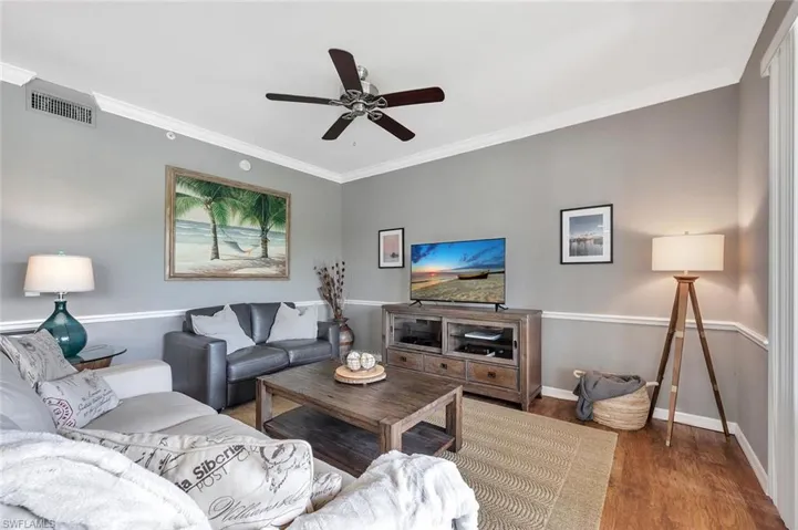 Living room with wood finished floors, ceiling fan, ornamental molding, and baseboards