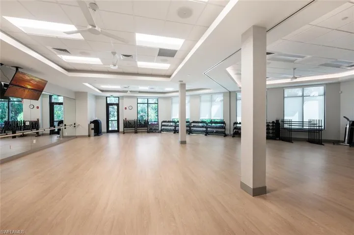 Gym with light wood finished floors, ceiling fan, a paneled ceiling, and a raised ceiling