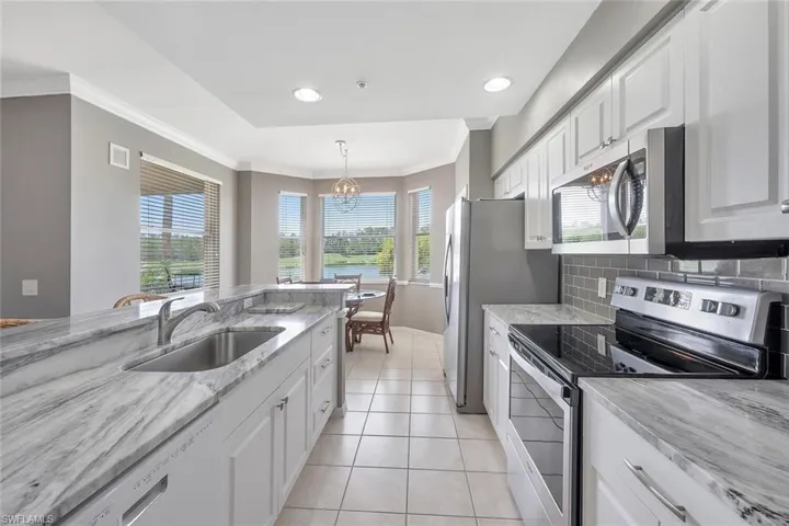 Kitchen featuring appliances with stainless steel finishes, a chandelier, a sink, white cabinetry, and ornamental molding