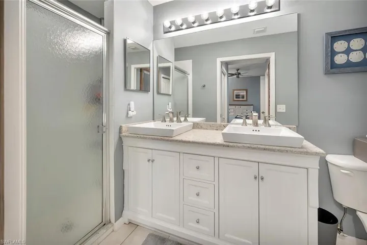 Full bathroom featuring a stall shower, toilet, double vanity, and a ceiling fan