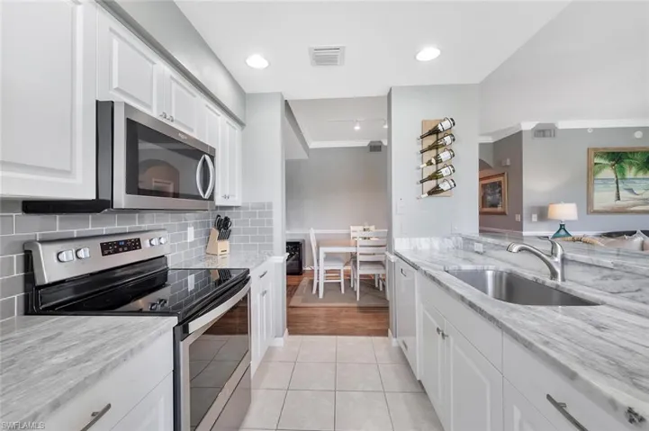 Kitchen with stainless steel appliances, a sink, white cabinetry, tasteful backsplash, and ornamental molding