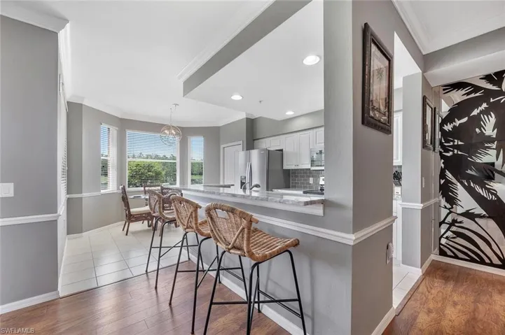 Kitchen featuring stainless steel refrigerator with ice dispenser, white cabinetry, a kitchen breakfast bar, light wood-style flooring, and crown molding
