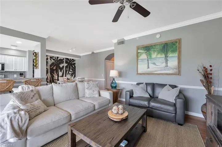 Living room featuring arched walkways, ceiling fan, baseboards, wood finished floors, and ornamental molding