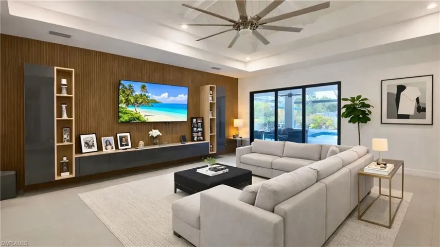 Virtually Staged  Living area featuring a ceiling fan, light tile patterned floors, wooden walls, and a tray ceiling