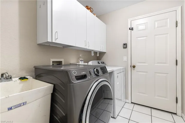 Laundry area featuring cabinet space, independent washer and dryer, light tile patterned floors, and a textured wall