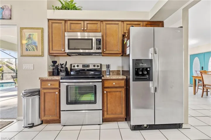 Kitchen with wood finish cabinets, stainless steel appliances, light stone countertops, and light tile patterned floors