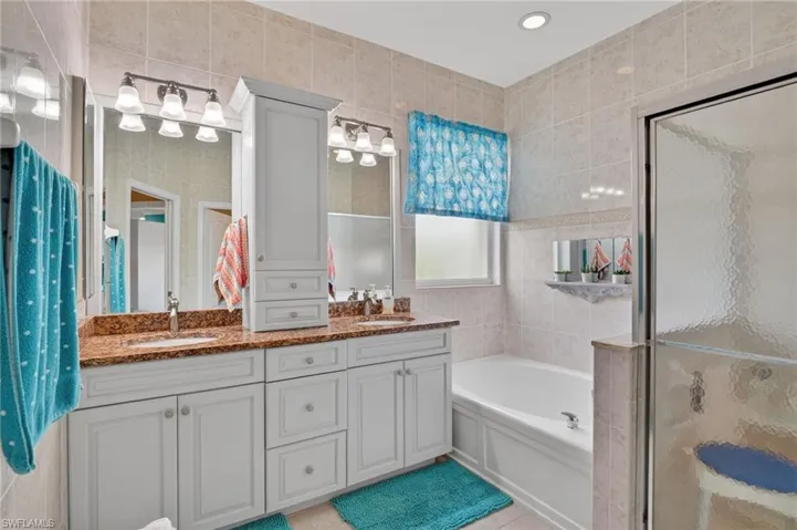 Bathroom featuring double vanity, a bath, tile walls, an enclosed shower, and recessed lighting