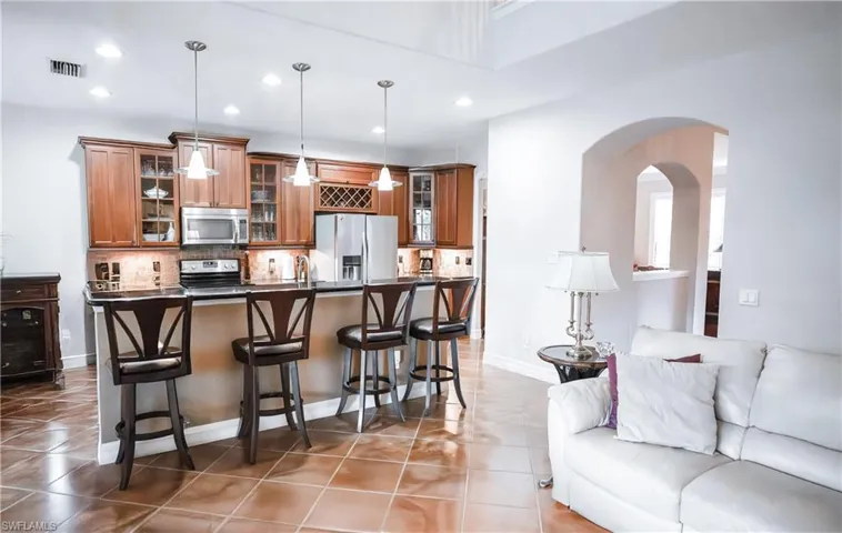 Kitchen with appliances with stainless steel finishes, decorative light fixtures, a kitchen breakfast bar, decorative backsplash, and dark tile patterned floors