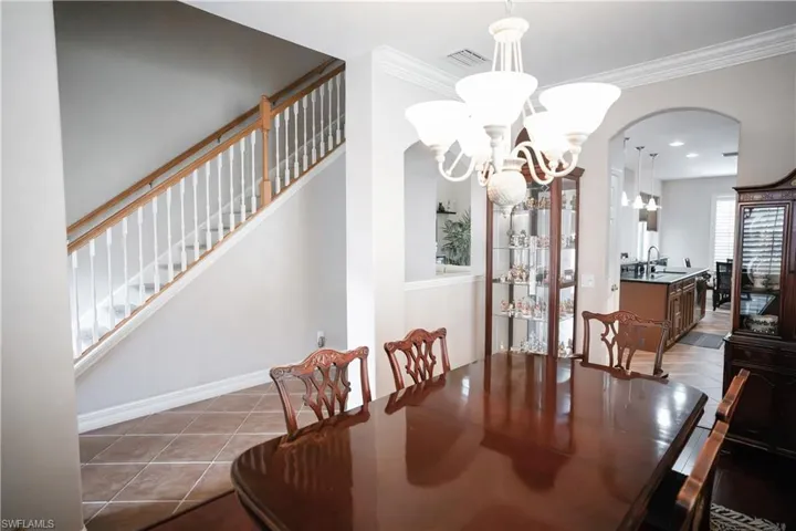 Tiled dining space with ornamental molding, sink, and a notable chandelier