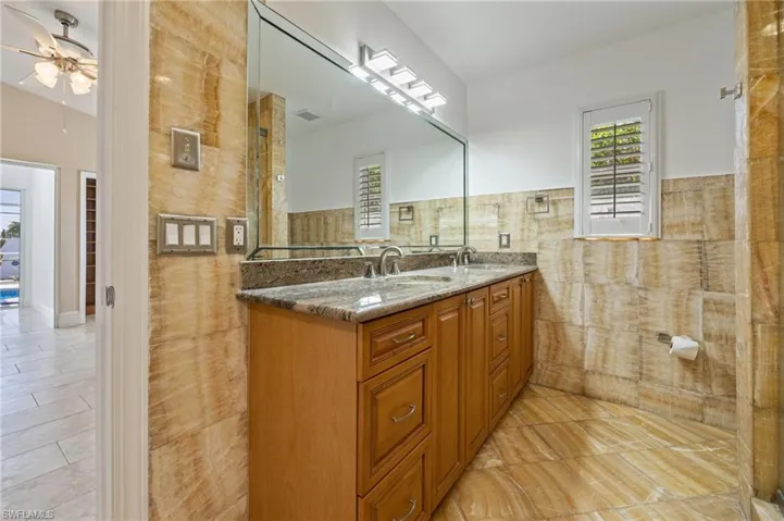 Full bathroom with ceiling fan, double vanity, tile walls, light tile patterned flooring