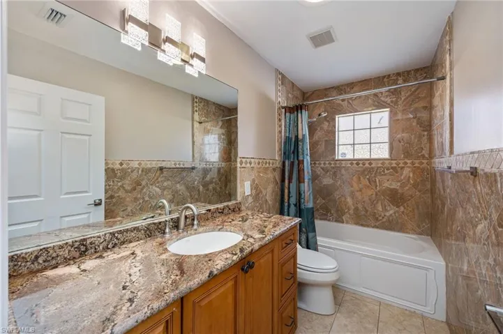Guest bathroom featuring vanity, shower / bath combo, tile walls, and light tile patterned floors