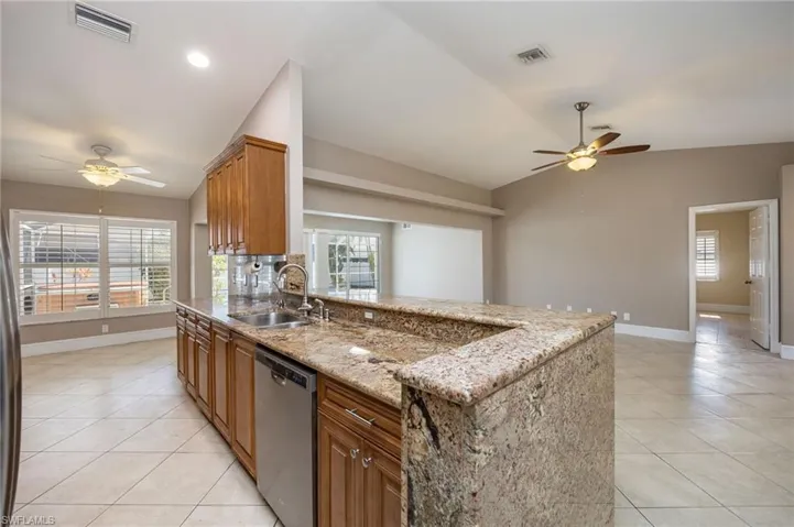 Kitchen featuring a ceiling fan, wood finish cabinets, light stone countertops, stainless steel dishwasher, and a peninsula