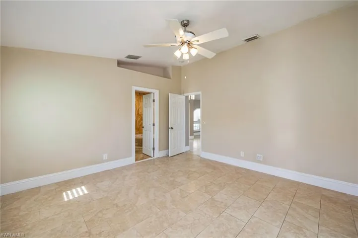 Primary bedroom featuring a ceiling fan, vaulted ceiling, and ensuite bathroom