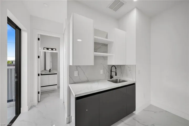 Kitchen with light stone counters, sink, white cabinetry, and tasteful backsplash