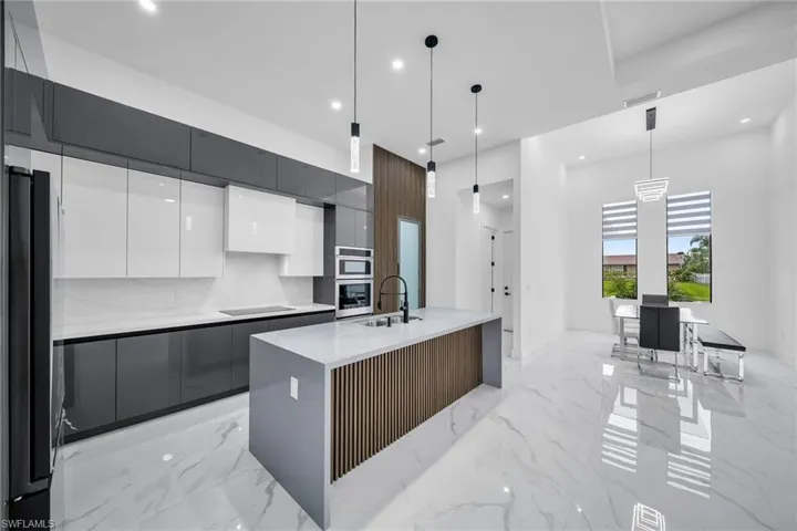 Kitchen featuring white cabinetry, stainless steel appliances, an island with sink, sink, and hanging light fixtures