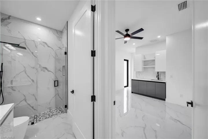 Bathroom featuring tiled shower, ceiling fan, toilet, and vanity