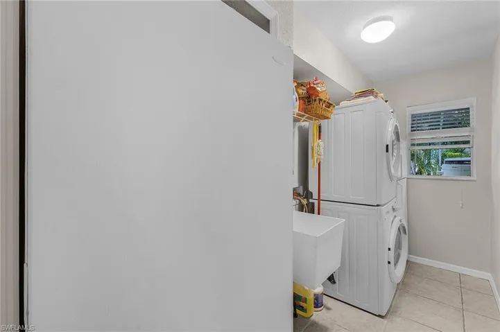 Washroom with light tile patterned floors, baseboards, laundry area, a sink, and stacked washer / drying machine