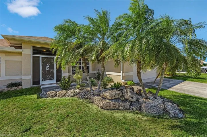 View of exterior entry with stucco siding, driveway, a lawn, and a garage