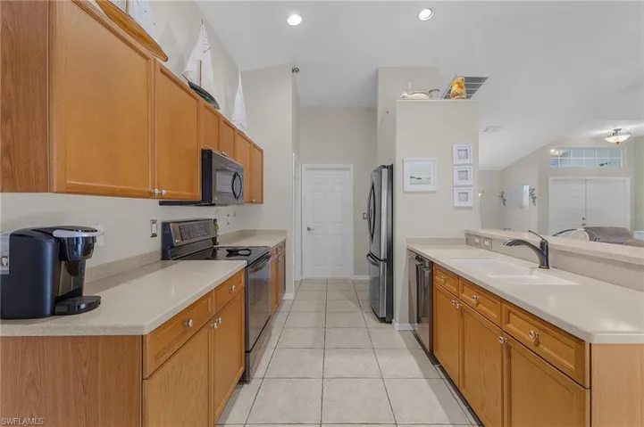 Kitchen with a peninsula, light tile patterned flooring, a sink, black appliances, and light countertops
