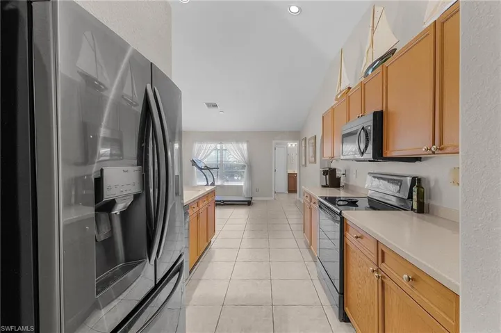Kitchen featuring baseboards, light tile patterned flooring, light countertops, vaulted ceiling, and appliances with stainless steel finishes