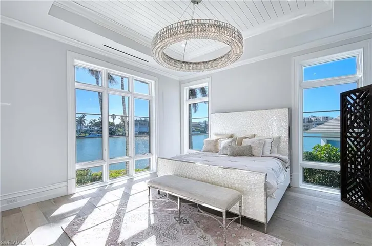 Bedroom with hardwood / wood-style floors, a notable chandelier, a water view, and multiple windows