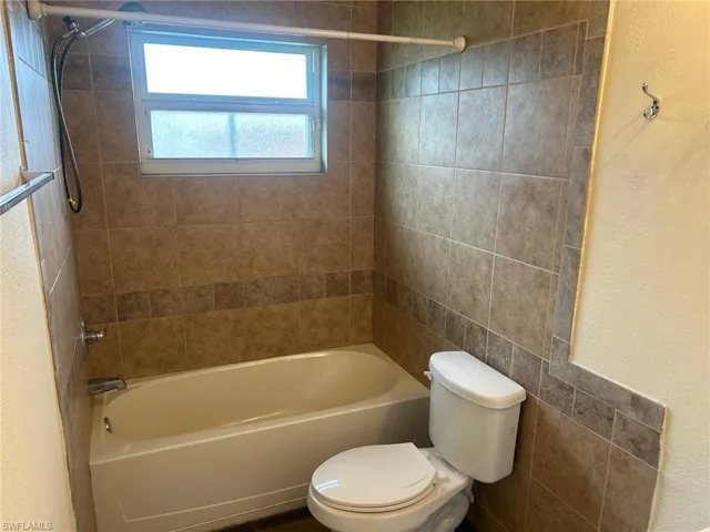 Bathroom with toilet, shower / bathtub combination, and a textured wall