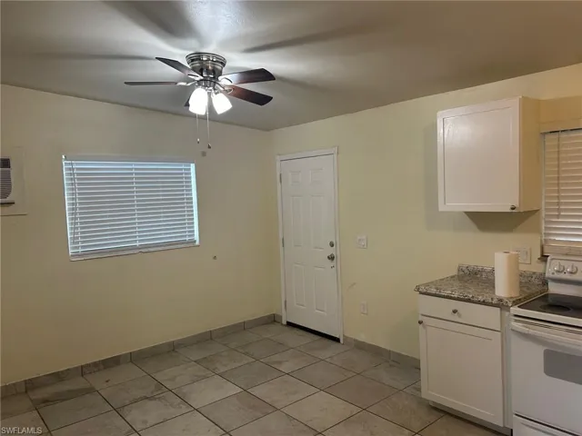 Kitchen with white range with electric stovetop, ceiling fan, white cabinets, light tile patterned floors, and stone counters