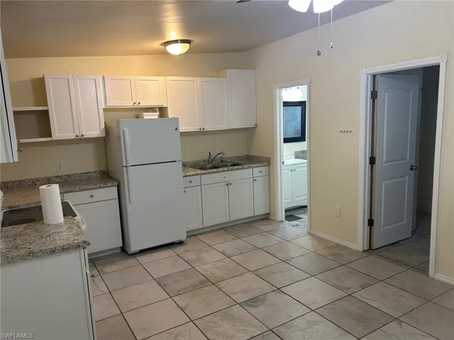Kitchen featuring freestanding refrigerator, open shelves, a sink, and white cabinetry
