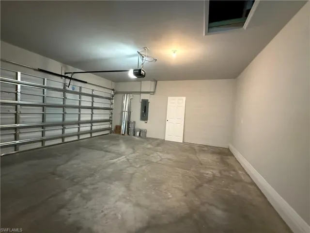 Garage featuring electric panel, a garage door opener, and baseboards