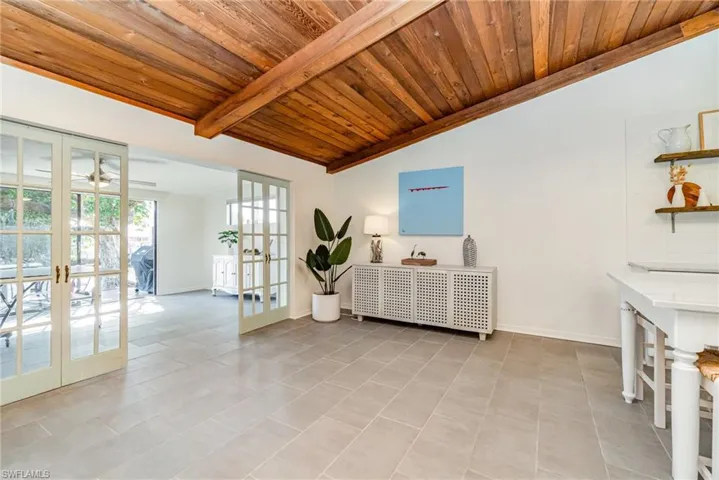 Tiled living area with vaulted ceiling with wood beams and french doors