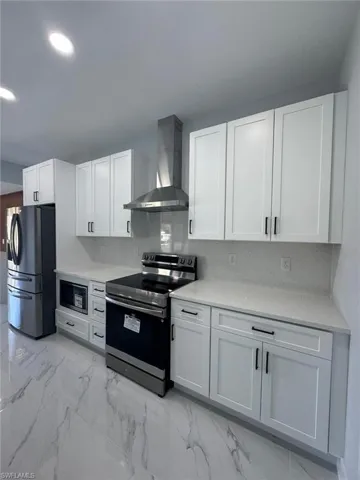 Kitchen with white cabinetry, appliances with stainless steel finishes, and wall chimney exhaust hood
