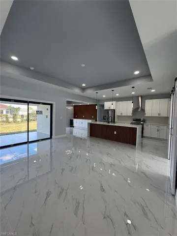 Kitchen featuring white cabinetry, wall chimney exhaust hood, a raised ceiling, a center island with sink, and stainless steel electric range