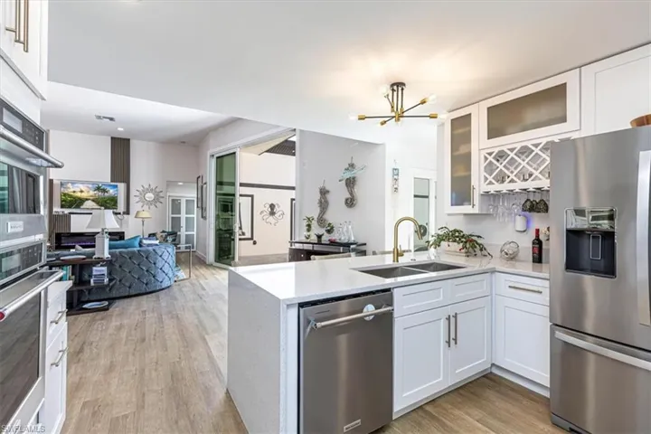 Kitchen featuring stainless steel appliances, white cabinets, light stone counters, a chandelier, and a peninsula
