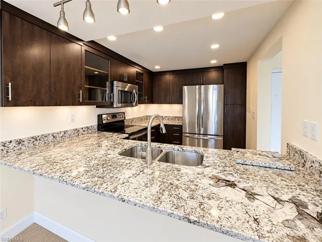 Kitchen featuring dark wood-finish cabinetry, stainless steel appliances, a double basin sink, under-cabinet lighting, and recessed ceiling lighting