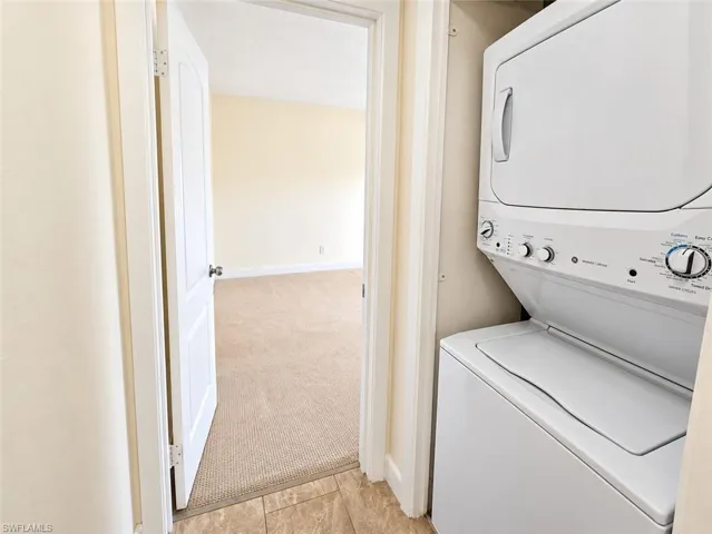 Stackable washer and dryer unit, neutral-toned wall paint, white interior doors, and carpeted flooring