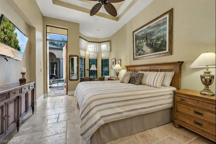 Bedroom featuring stone tile flooring, a raised ceiling, arched walkways, and ceiling fan