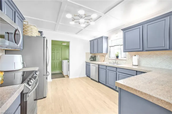 Kitchen with stainless steel appliances, coffered ceiling, light wood-type flooring, decorative backsplash, and a chandelier